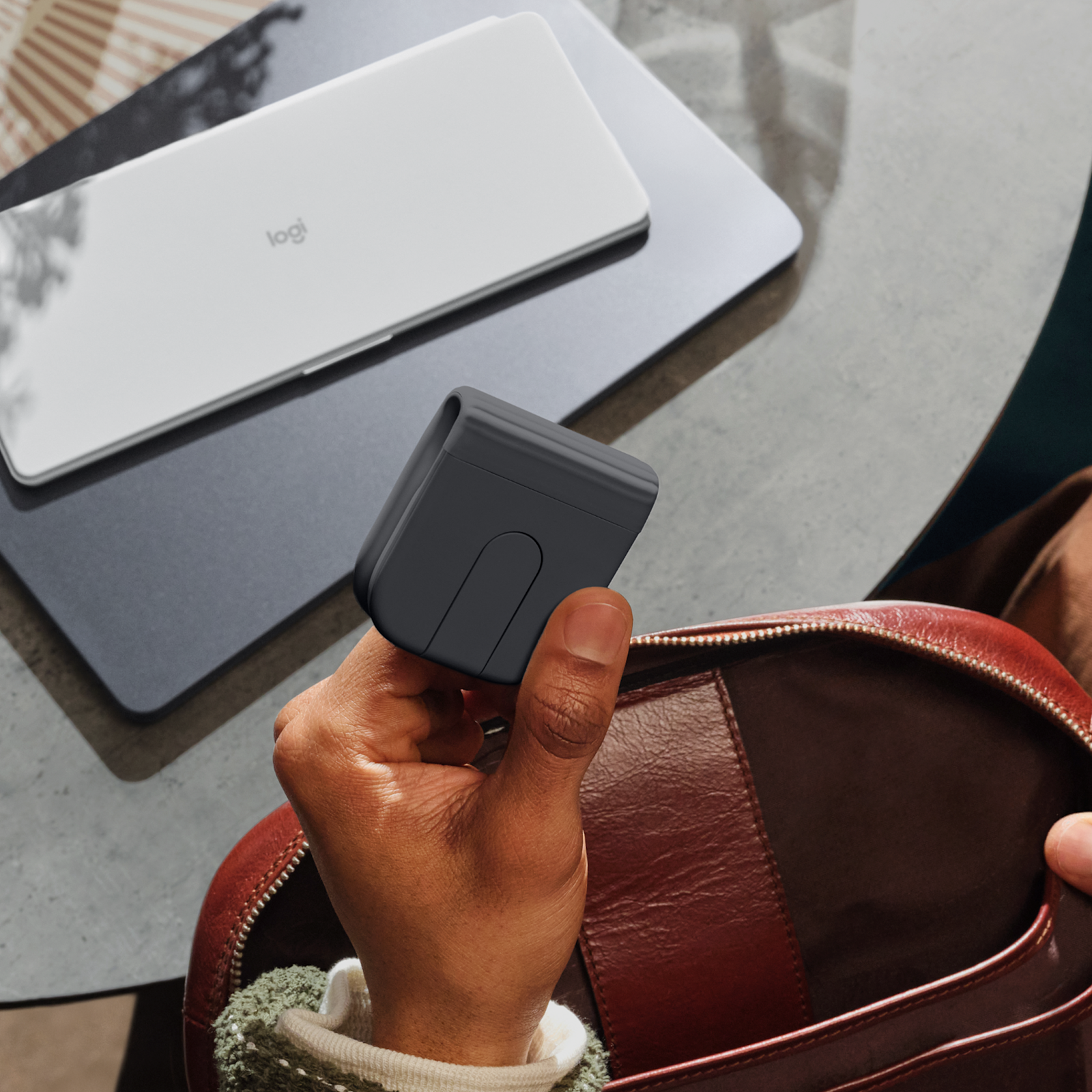 Logitech Mobi Fold mouse Graphite folded in the hand next to a bag